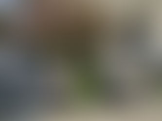 Duas esculturas em bronze: cavaleiro de armadura segura um elmo; ao lado, rei coroado inclina-se sobre uma mesa de pedra, com árvores em flor ao fundo.