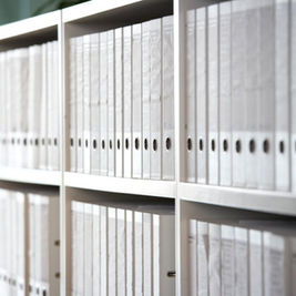 Prateleiras de arquivo repletas de dossiês brancos alinhados, simbolizando a vasta coleção de documentos históricos reunidos no pós-guerra.