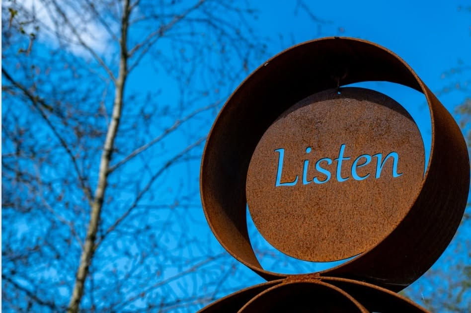 Placa circular com a palavra “Listen” integrada numa estrutura metálica, evocando a escuta e a atenção à leitura.