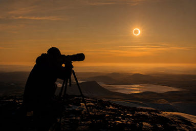 A photographer captures a breathtaking solar eclipse above a picturesque mountain landscape