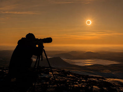 A photographer captures a breathtaking solar eclipse above a picturesque mountain landscape