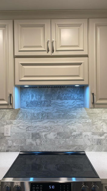 Complete kitchen renovation featuring a transformation from dark wood cabinets and granite countertops to a bright, modern design with cream shaker-style cabinets, quartz countertops, stainless steel appliances, gray stone backsplash, and wood-look flooring