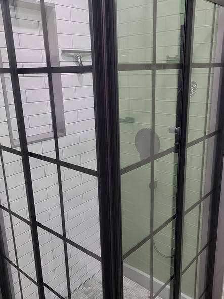 Black framed glass walk-in shower enclosure with green and white subway tile walls in Collegeville PA bathroom renovation
