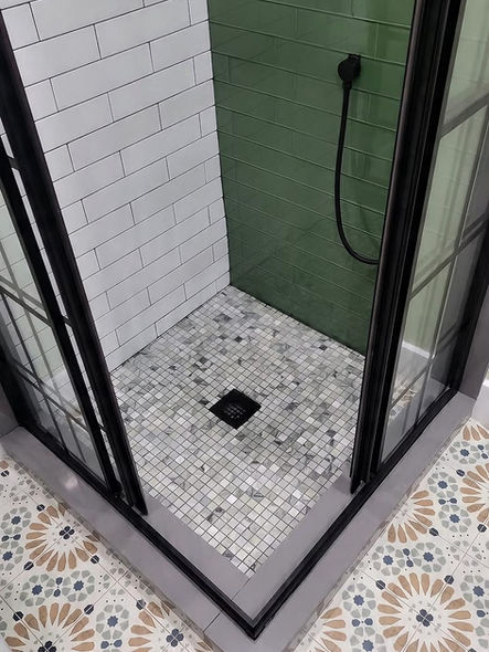Curbless walk-in shower with mosaic tile floor, matte black drain, green subway tile accent wall, and black framed glass enclosure in Collegeville PA