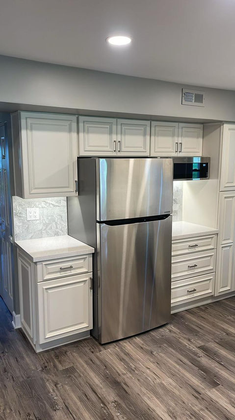 Complete kitchen renovation featuring a transformation from dark wood cabinets and granite countertops to a bright, modern design with cream shaker-style cabinets, quartz countertops, stainless steel appliances, gray stone backsplash, and wood-look flooring