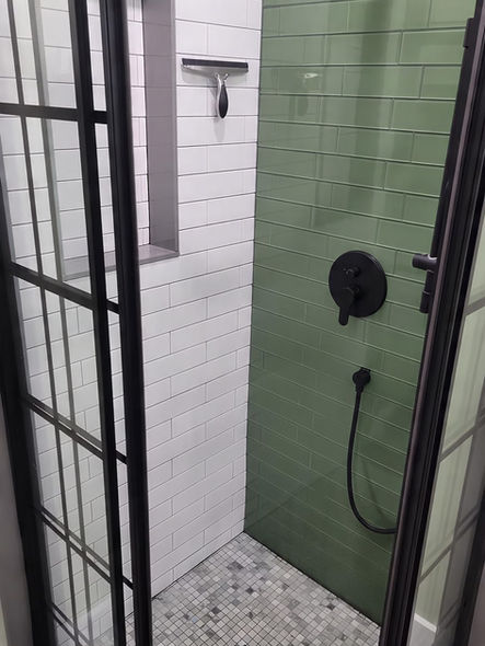 Before and after curbless walk-in shower remodel in Collegeville PA featuring green subway tile, black framed glass enclosure, mosaic shower floor, and matte black fixtures