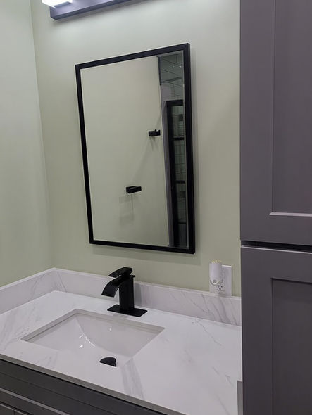 Custom gray vanity with quartz countertop, black faucet, framed mirror, and modern lighting in remodeled Collegeville PA bathroom