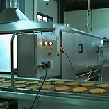 "Imagen de una línea de producción de hamburguesas con diferentes estaciones de trabajo y maquinarias, incluyendo cintas transportadoras, máquinas para dar forma a las hamburguesas, herramientas para cortar y rellenar panes, y estaciones de empaquetado. Los trabajadores están presentes en varias etapas de la línea para monitorear el proceso y asegurar la calidad del producto final