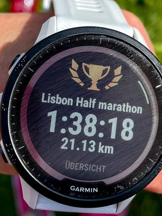 Eine Läuferin trägt eine Smartwatch, auf deren Bildschirm „Halbmarathon von Lissabon“ angezeigt wird.