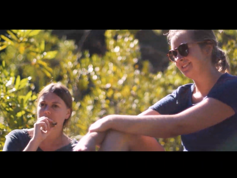 Two white women sitting at a lush green riverbank.