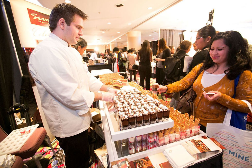 A smiling man in a chef's coat stands next to a woman at a wedding show, showcasing their culinary offerings.