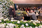 Engaged couple posing in front of a wall of flowers at a bridal show.