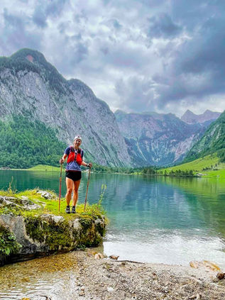 Eine Trailrunnerin genießt auf einem großen Felsen stehend den Blick auf den Königssee.