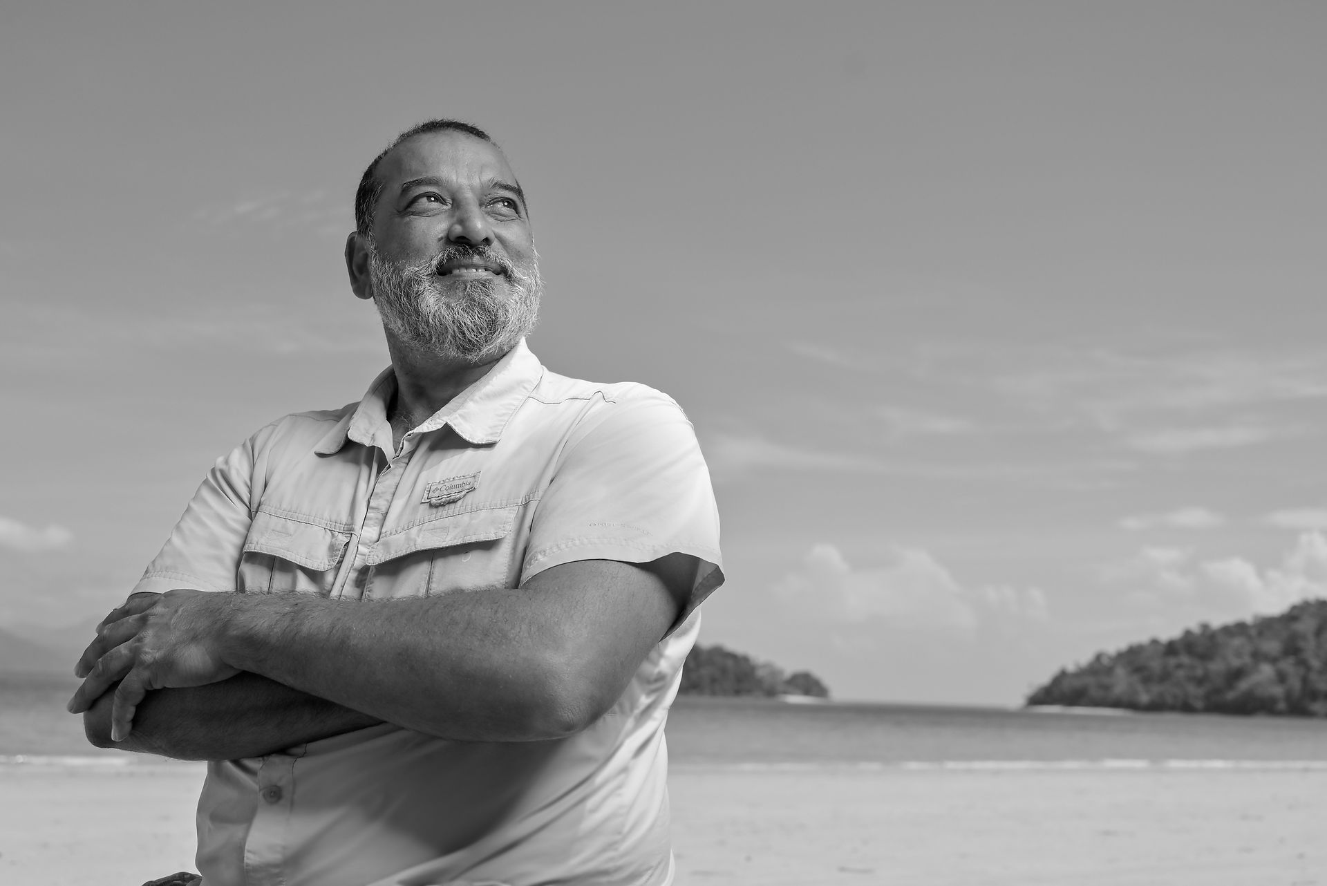 Man smiles on beach, arms crossed