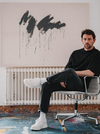 Man in black shirt sits in chair, abstract art behind