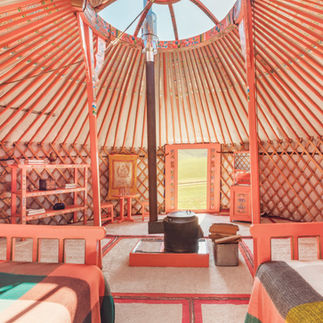 Interior of a cozy yurt with beds, shelves, and a wood-burning stove