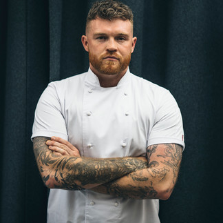Chef portrait: arms crossed, tattooed, wearing a white chef's jacket