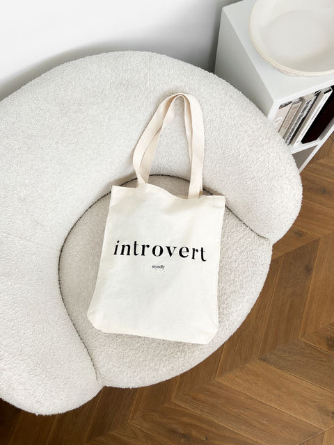A tote bag that reads "Introvert" laying on a beautiful white boucle armchair.