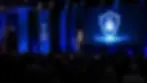 Professional keynote speaker at conference stage podium with cybersecurity screen display and packed auditorium audience.