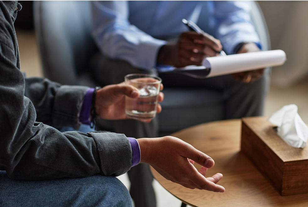 Close-up of a therapy session showing one person holding a glass of water and gesturing while another takes notes on a clipboard, symbolizing mental health support and compassionate communication.