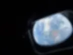 Silhouette of a person gazing at Earth from a spaceship window, displaying vast blue oceans and swirling white clouds in space.