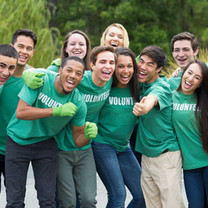 Group of smiling volunteers wearing green shirts with the word VOLUNTEER.