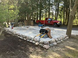 A gravel parking space with retaining rocks lining it and a truck and equipment pictured nearby