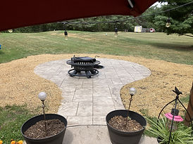 A white hardscape with a fire pit on it, surrounded by soil and seeding to complete the space