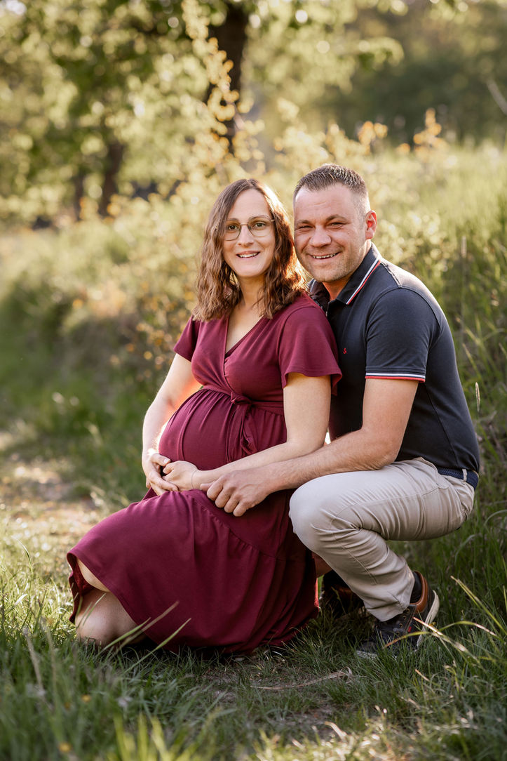 Werdende Eltern sitzen eng beieinander und halten liebevoll den Babybauch.