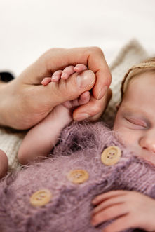 Schlafendes Neugeborenes in einem lila Strickoutfit bei einem professionellen Newbornshooting