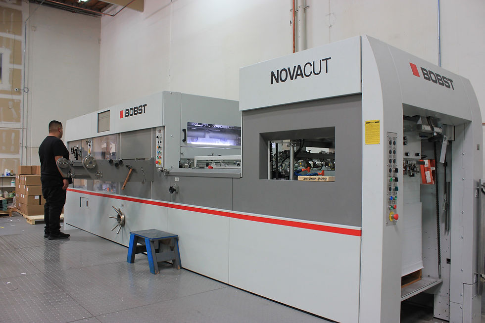 Operator running a Bobst die-cutting machine to cut printed sheets of retail folding carton boxes