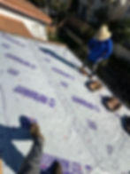 Two workers are on a sloped house roof covered with synthetic roofing underlayment