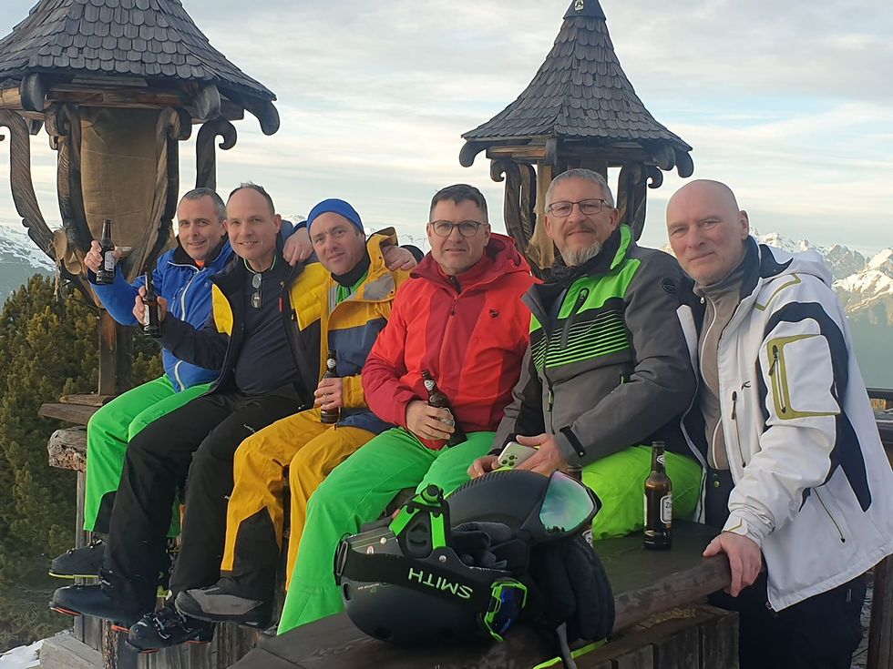 Sechs Männer sitzen auf einer Bank mit Bergen im Hintergrund. Jungsenioren sind hier.