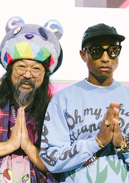 takashi murakami and pharrell williams posing in front of art with prayer hands