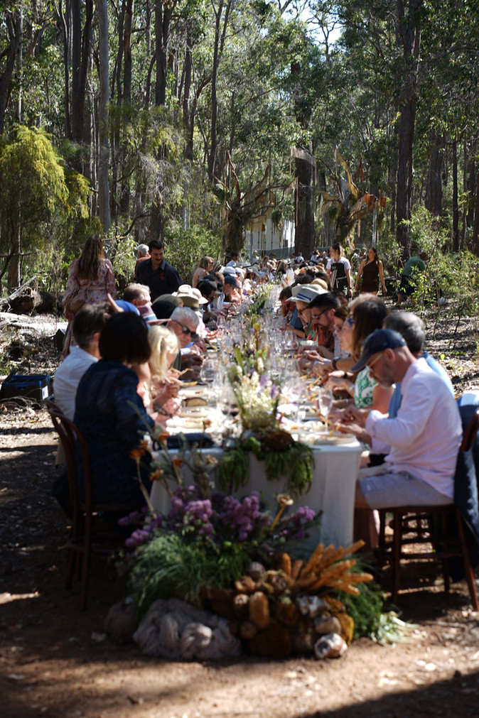 Long table under karri trees at Tanah Marah during Nature’s Table, with guests enjoying a four‑course feast crafted from seasonal ingredients and paired with Margaret River wines