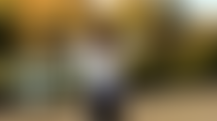 A woman standing outdoors with arms outstretched toward autumn trees, embracing freedom and joy in nature. Megan Haggett created this image.