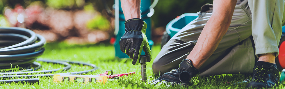 Worker installing underground drainage in a grassy landscape area.