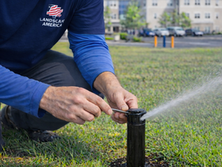 Worker adjusting a sprinkler head in a grassy area while water sprays across the lawn.