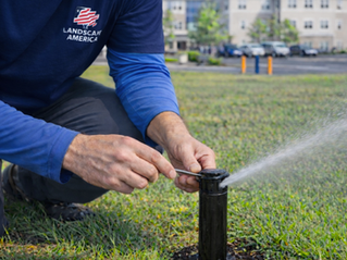 Worker adjusting a sprinkler head in a grassy area while water sprays across the lawn.