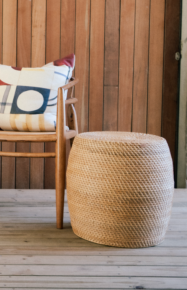 Medium natural rattan drum stool with handwoven texture and organic shape next to a chair