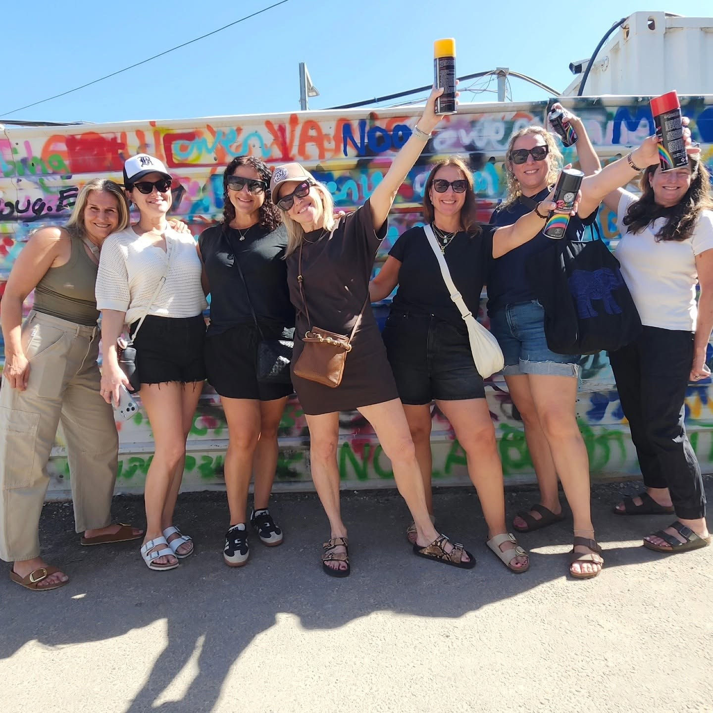 A group raising spray cans in front of a graffiti wall in Tel Aviv