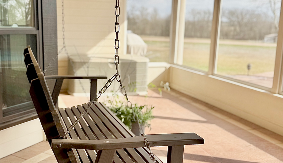 Wooden porch swing on a sunlit screened-in patio.