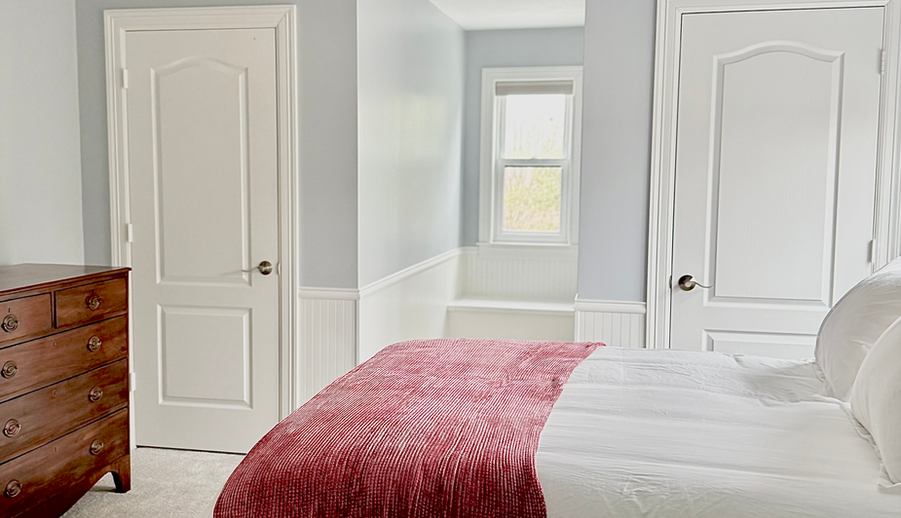 Bedroom with white bed, red throw, and ceiling fan.
