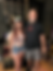 Ashley Wineland and Bryan Kuban standing shoulder to shoulder inside of a studio room with guitars and amps behind them