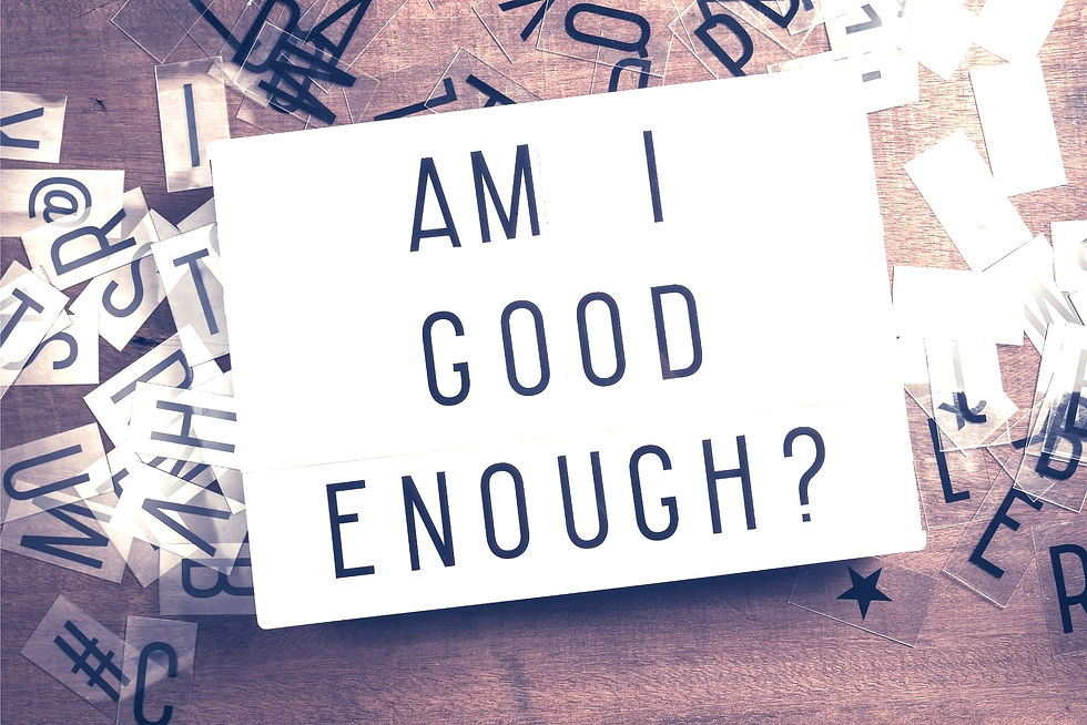 Lightbox with "AM I GOOD ENOUGH?" text on wooden table. Transparent letters scattered around. Reflective and introspective.