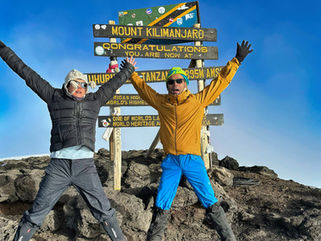 A man and a woman with arms extended at the summit of Mt Kilimanjaro