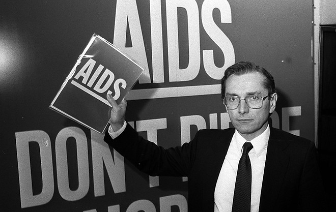 Health Secretary Norman Fowler, in London in 1986, in front of a poster reading "Aids Don't Die Of Ignorance"