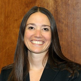 Smiling woman with long brown hair in front of a wooden background.