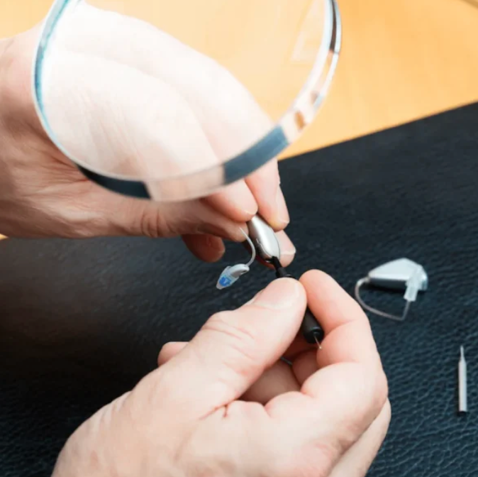 Hands examining a hearing aid with a magnifying glass