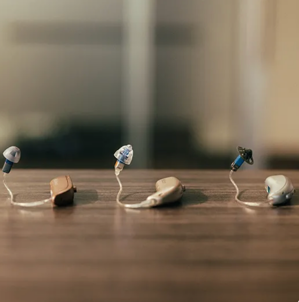 Three different hearing aids on a wooden surface.